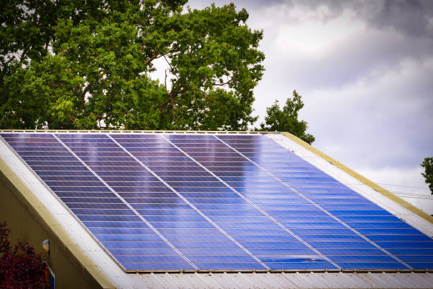 A rooftop with solar panels installed, set against a backdrop of trees and a cloudy sky.
