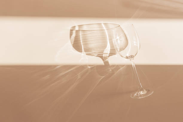 istock One empty wineglass sparkling at sunlight, dark shadow and shiny reflection, sun flare light effect on table. Crystal glass top view, neutral pastel abstract beige background, copy space 2167038019