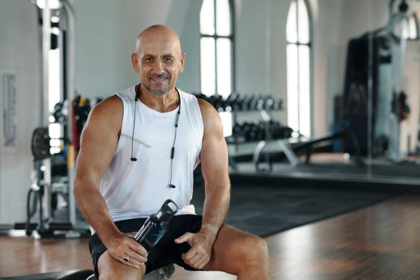 Portrait of sport instructor with bottle of water smiling at camera while sitting in sport gym