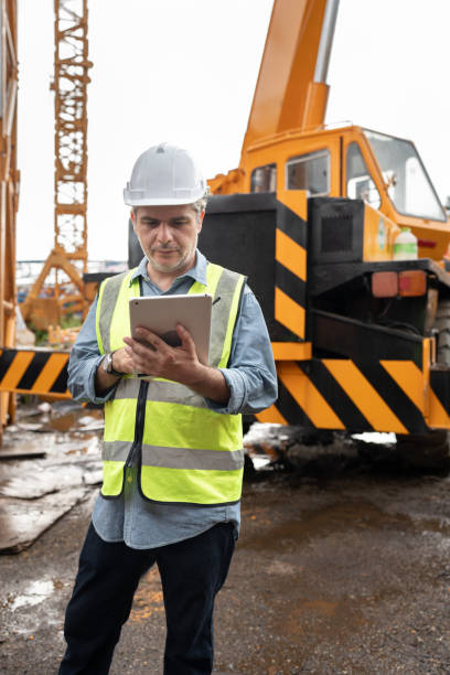 istock Caucasian mature engineer man worker use tablet computer and walkie talkie working with crane truck and spare crane background 2167042330