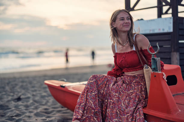 Young woman sitting on a lifeguard's boat at a Tuscan beach. \nSunny summer vacations evening.\nShot with Canon R5