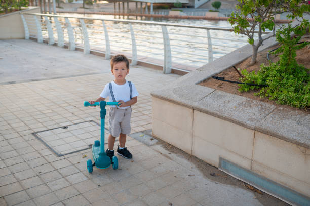 Charming toddler in a summer outfit is having fun while riding a blue kids three wheeled scooter outdoors. Children's sports, vehicle for active children, free activity for boys and girls