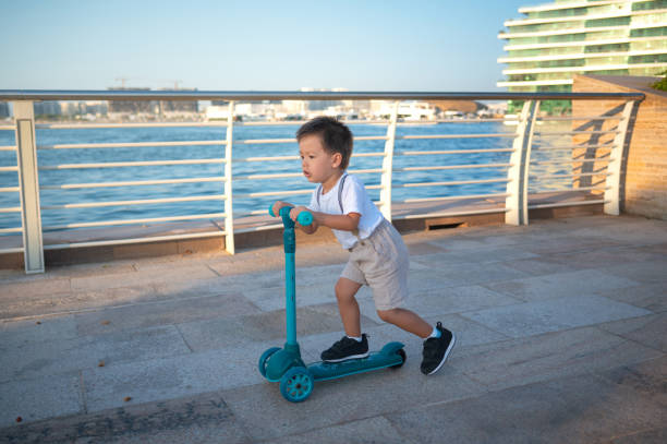 istock Little two year old boy riding a three wheeled children's scooter by waterfront 2167057808