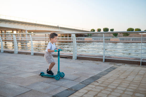 istock Little two year old boy riding a three wheeled children's scooter by waterfront 2167057816