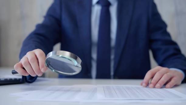 istock Businessman is carefully examining financial documents with a magnifying glass, highlighting the importance of thorough analysis in business. Audit and taxes 2167058073