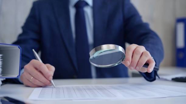 istock Businessman is carefully examining financial documents with a magnifying glass, highlighting the importance of thorough analysis in business. Audit and taxes 2167060178