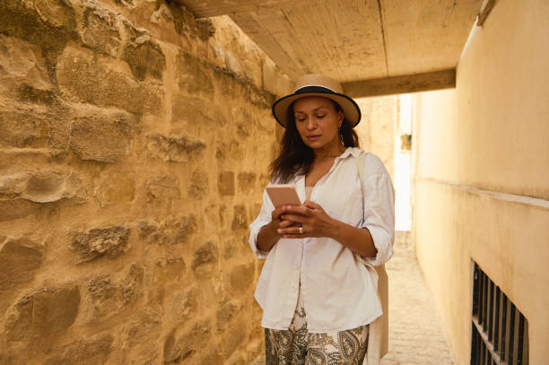 istock Woman exploring ancient alley while using smartphone in sunlit passageway, showcasing travel adventure and modern technology 2167065918