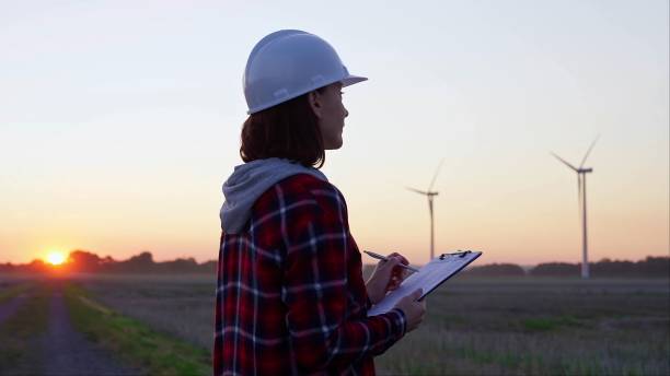 istock Woman engineer is taking notes on a clipboard on a field with wind turbines, as the sun sets in evening. Clean energy and engineering 2167067639