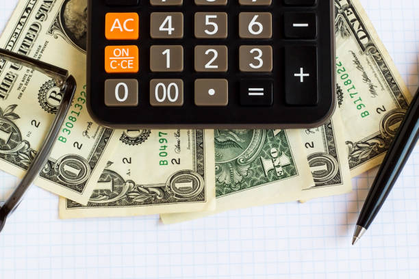 Above view of one dollar US bills on white plaid  paper with calculator,pen and glasses.Conceptual image of finance