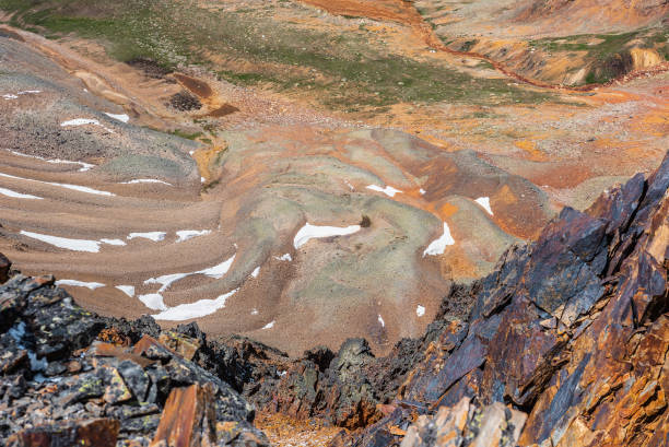 istock Scenic dizzy top-down view from precipice edge with sharp rocks to unusual multicolor stony valley with iron river in sunlight. Colorful awesome alpine scenery with snow in multi-color hilly valley. 2167078912