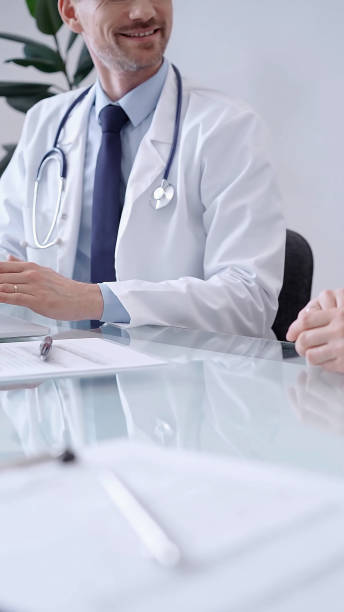 istock Doctor consulting patient. Male physician is gesturing above a clipboard while talking with a woman in a clinic, close up 2167079663