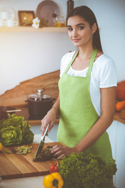 istock An attractive young dark-haired woman preparing delicious fresh vegetarian salad while standing and smiling in sunny kitchen. Cooking and householding concepts 2167081663