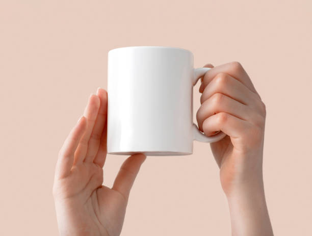 Woman holds a ceramic white cup in her hands. Mockup coffee mug in on beige background
