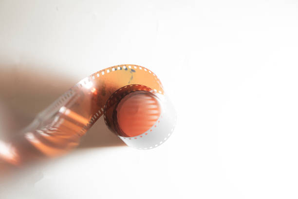 A close-up of a curled film strip against a white background, showcasing the perforations and the orange tint of the film.