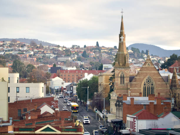 Horizontal high angle photo of part of the city of Hobart with hills, distant houses, city buildings, busy Bathurst St and the tall spire of the Hobart Full Gospel Central Church standing out against a Winter sky.