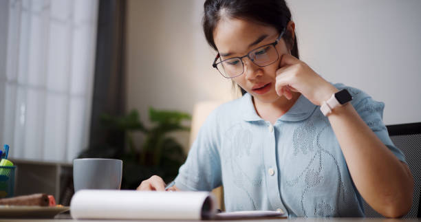 istock Young woman taking notes in notebook sitting at table at home. 2167094233