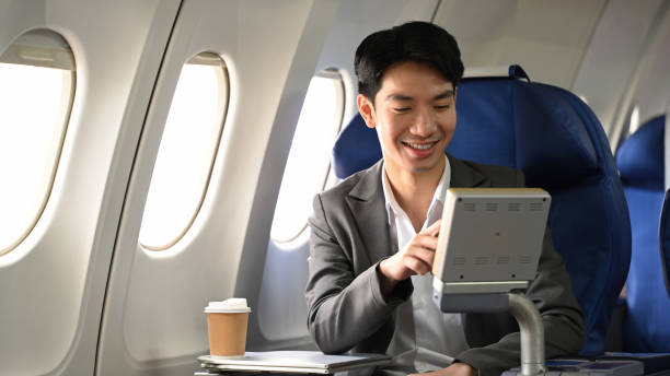 istock Smiling young businessman in a suit pointing at something on the screen on an airplane seat 2167094708