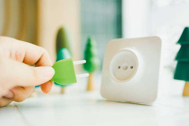 Businessman holding a green plug plugged into a socket surrounded by tree models, concept of carbon credit, using natural energy, generating electricity from nature.
