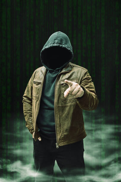 istock Faceless man, hooded cybercriminal terrorist, anonymous hacker standing on a dark green background with a smoke 2167112628
