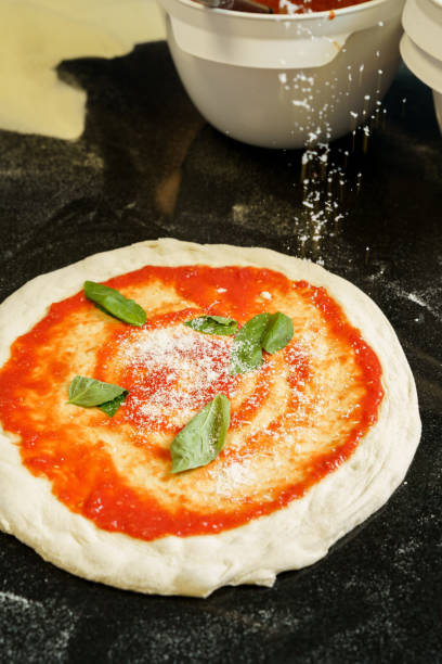 istock A chef preparing a pizza with tomato sauce and spreading parmesan cheese 2167123351