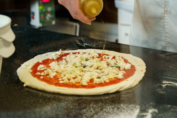 istock A chef preparing a pizza with tomato sauce and mozzarella cheese, spreading olive oil on pizza 2167123355