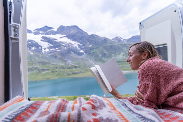 istock Woman Reading in Campervan Bed with Panoramic Mountain Lake View 2167125656