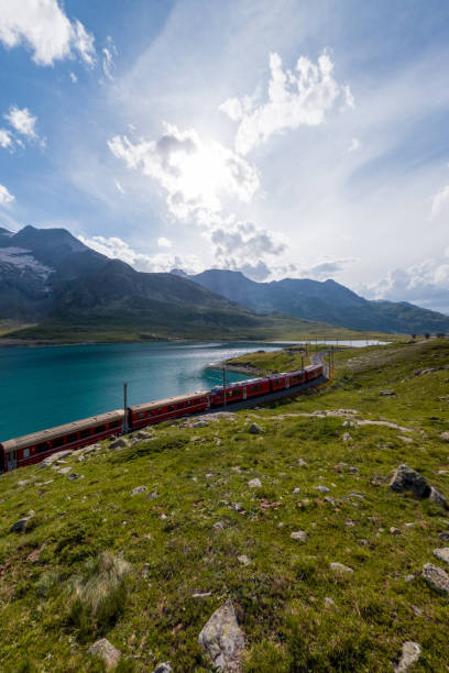 istock Red Train Curving Alongside Scenic Alpine Lake with Mountain Backdrop 2167128244