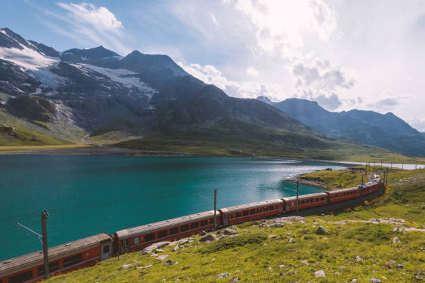 istock Red Train Curving Alongside Scenic Alpine Lake with Mountain Backdrop 2167128446