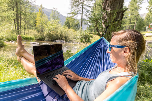 istock Woman Typing on Laptop While Relaxing in Hammock by Stream 2167130299