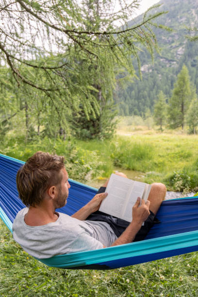 istock Man Relaxing in Hammock Reading a Book in Forest 2167131405