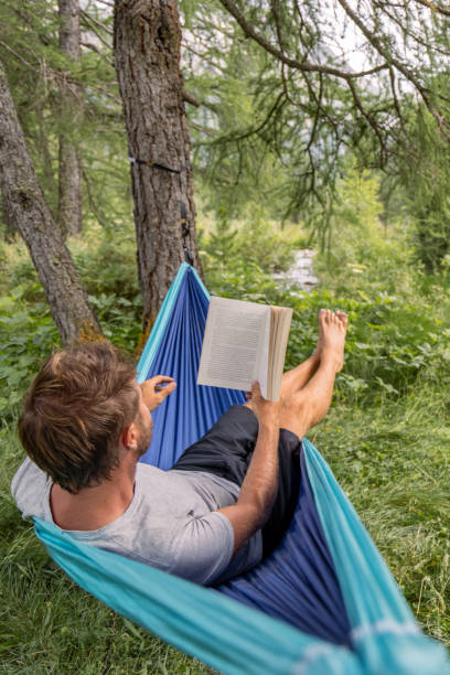 istock Man Reading a Book in Hammock by Forest Stream 2167131884