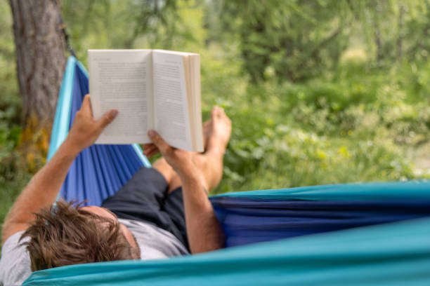 istock Man Reading a Book in Hammock by Forest Stream 2167131974