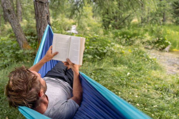 istock Man Reading a Book in Hammock by Forest Stream 2167131975