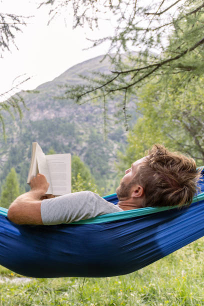 istock Man Relaxing in Hammock Reading a Book in Scenic Forest 2167132104
