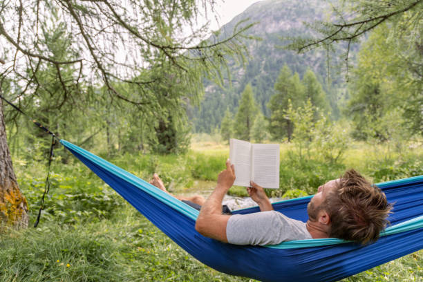 istock Man Relaxing in Hammock Reading a Book in Scenic Forest 2167132151