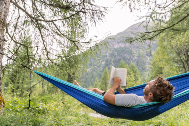 istock Man Relaxing in Hammock Reading a Book in Scenic Forest 2167132155