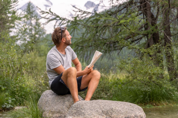 istock Man Enjoying a Book While Sitting on a Rock in Nature 2167132816
