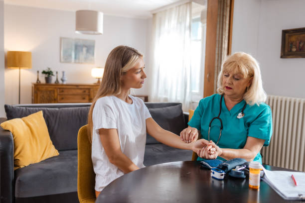 At Home Exam By A Nurse Senior nurse is conducting an at home visit to a young woman, checking her vitals and doing a general exam. Doctor taking blood pressure of a british patient in a home setting stock pictures, royalty-free photos & images