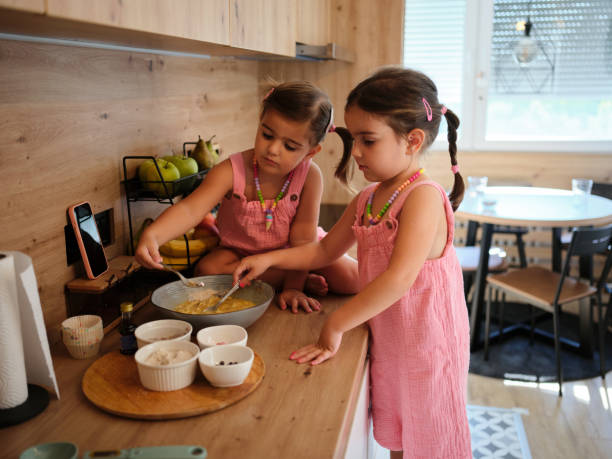 istock Two young girls are preparing dough for baking on the kitchen counter. Various baking ingredients and tools can be seen around them, signifying a baking activity. 2167135667