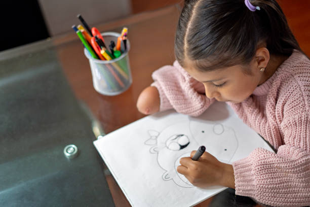 Latina girl at table with disability doing homework at home, the girl has an amputated arm and is drawing in a notebook.