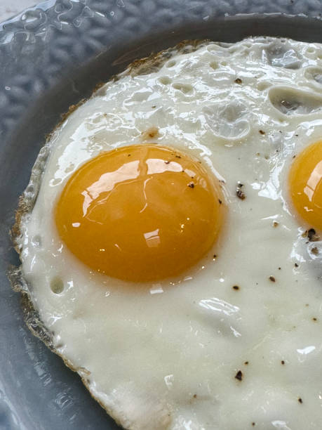 istock Full frame image of blue plate with floral patterned rim containing two merged cooked sunny side up fried eggs seasoned with cracked pepper corn, elevated view 2167141749