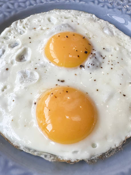 istock Full frame image of blue plate with floral patterned rim containing two merged cooked sunny side up fried eggs seasoned with cracked pepper corn, elevated view, focus on foreground 2167141767