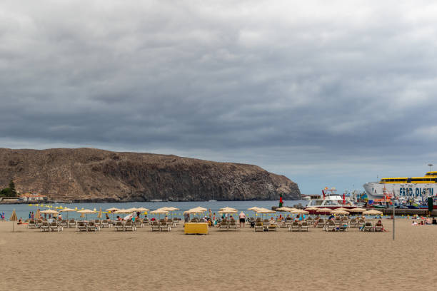 istock Cloudy day at the beach with empty sun loungers and umbrellas, with cliffs in the background in Los Cristianos, Tenerife. 2167149948