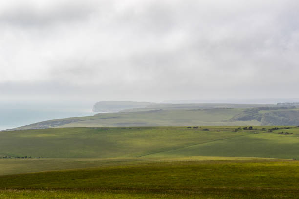 istock Rolling green hills with a distant cliff overlooking the sea under a cloudy sky at Seven Sisters, England. 2167159916