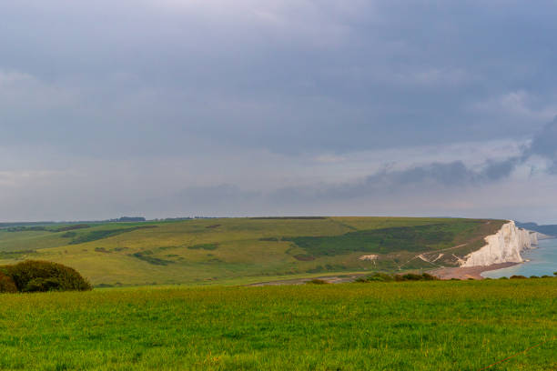 Rolling green hills with white cliffs under a stormy sky.