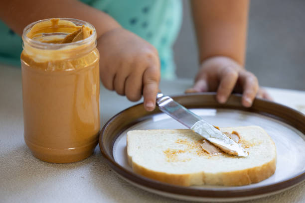 A child is spreading a peanut butter on a slice of bread