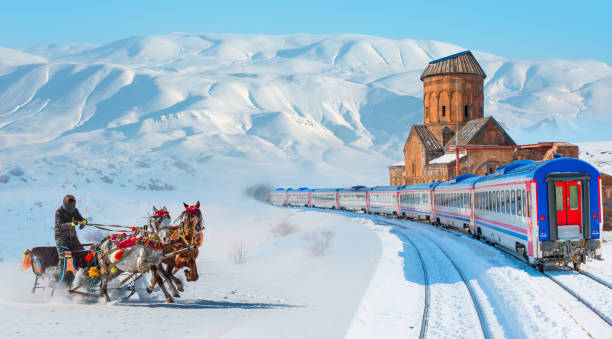 istock Red diesel train (East express) in motion at the snow covered railway - Horses pulling sleigh in winter - Ani Ruins, Ani is a ruined and  medieval Armenian city - Kars, Turkey 2167162764