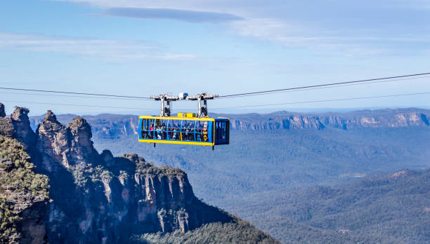 Katoomba, Australia, July 28, 2023. A cable car full of visitors hanging in the air with  famous Three Sisters cliffs at background in Australia Blue Mountains National Park.