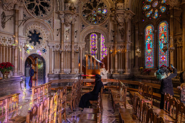 Montserrat, Barcelona, Spain - January 7, 2024:  Visitors in the beautiful Throne's Chapel of Basílica de Montserrat,  Santa Maria de Montserrat Abbey, with colorful light spots from stained glass windows.  HDR encoded.