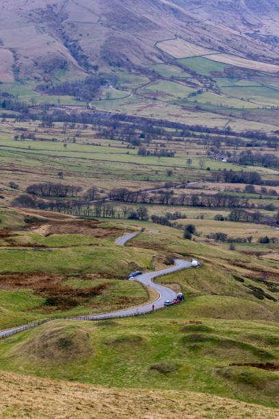istock Winding road through a hilly countryside landscape with scattered trees and fields, under a cloudy sky in Peak District, England. 2167168544